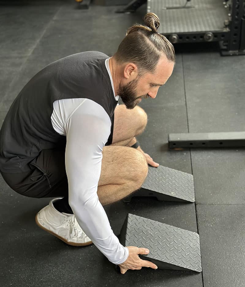 Bryan Crossley, DC personal trainer adjusts squat wedges to help his client with an assisted squat exercise program